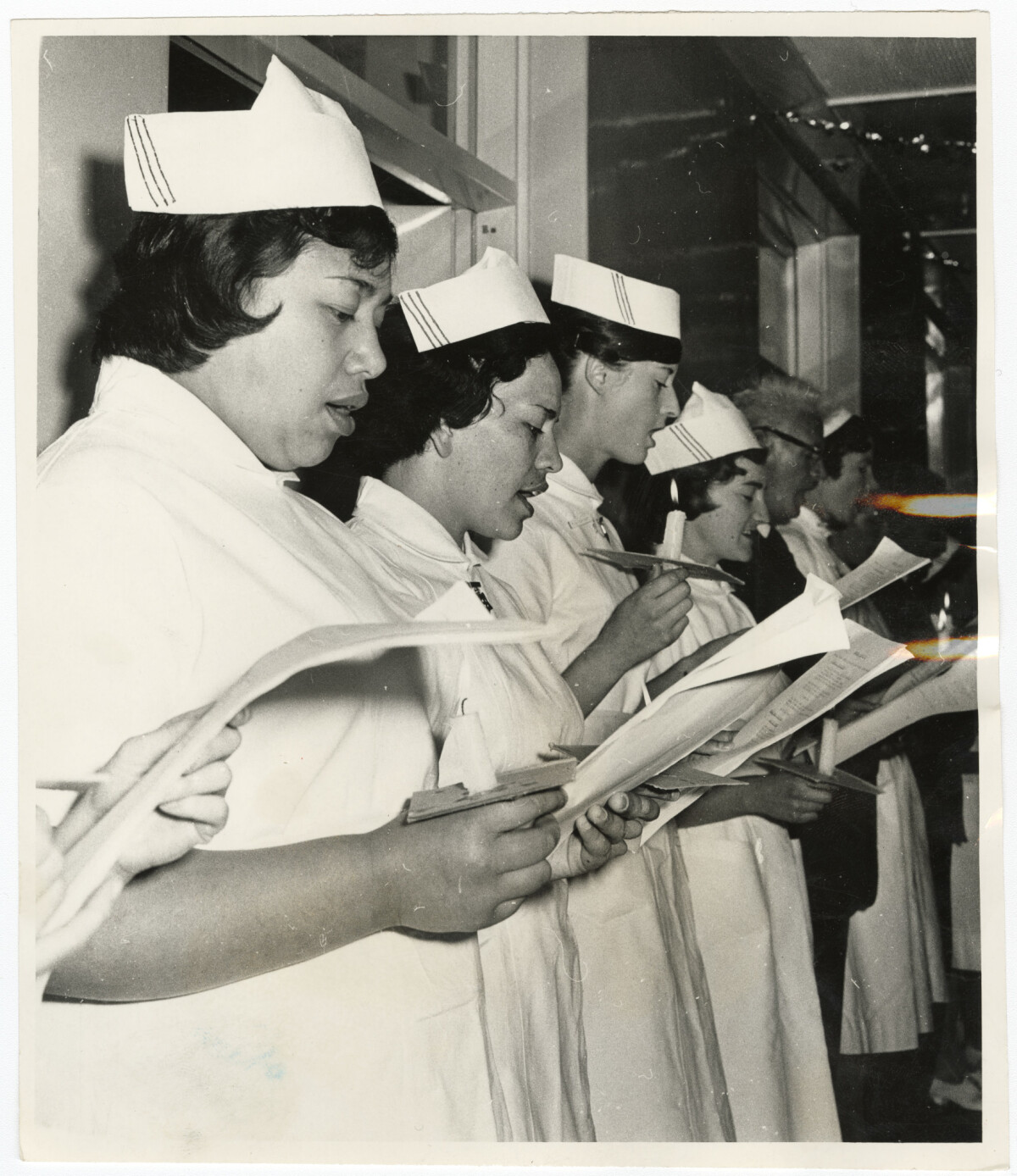 Black and white photo showing a line of nurses holding songbooks and candles, singing Christmas carols, 1963