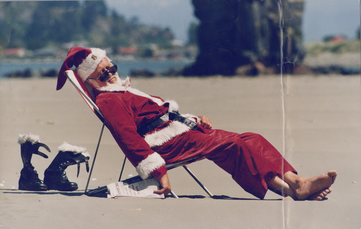 Photo of a man dressed as Santa Claus reclining in a folding chair on a beach