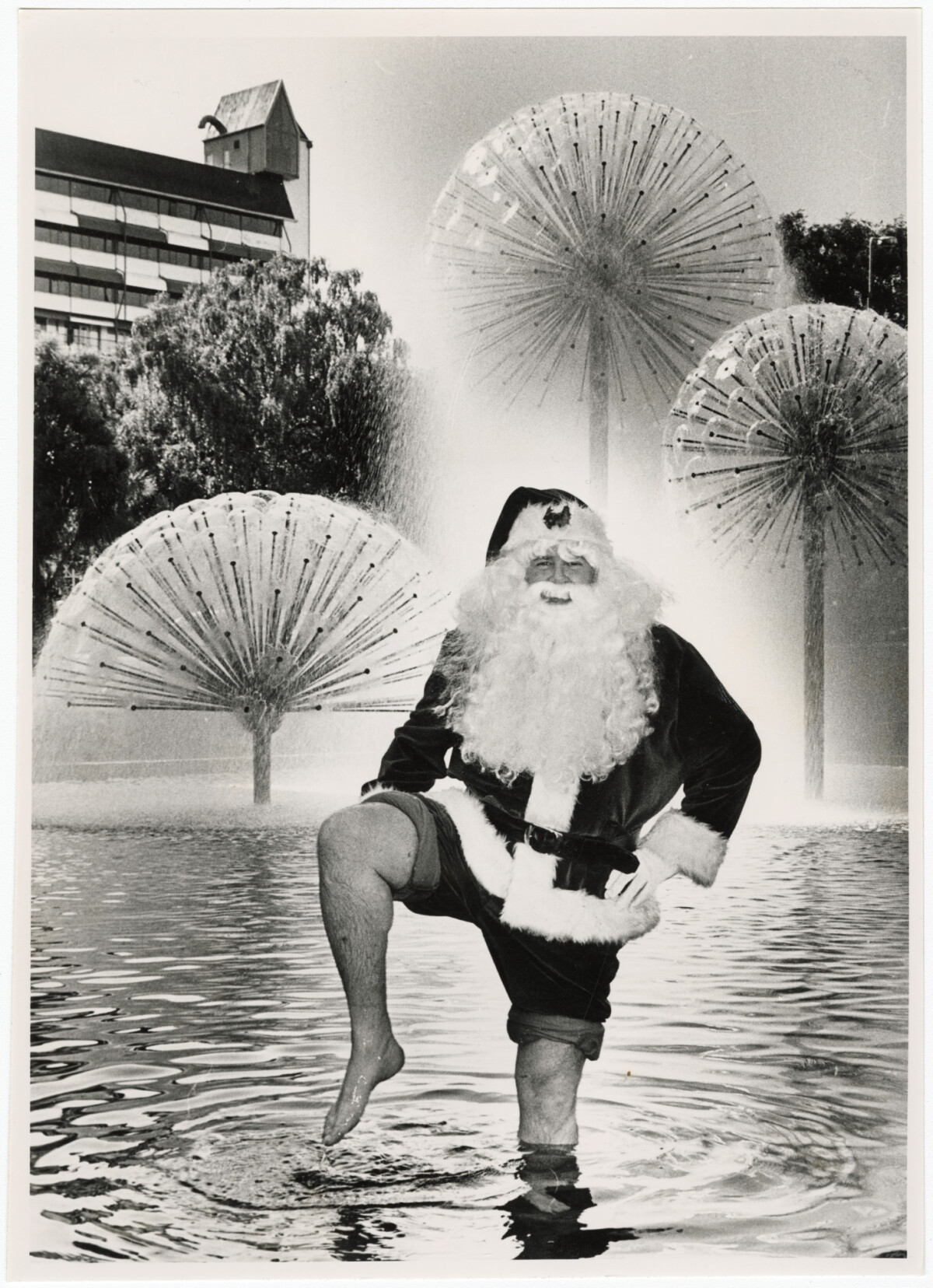 Black and white photo of a man dressed as Santa Claus standing in a fountain, 1984